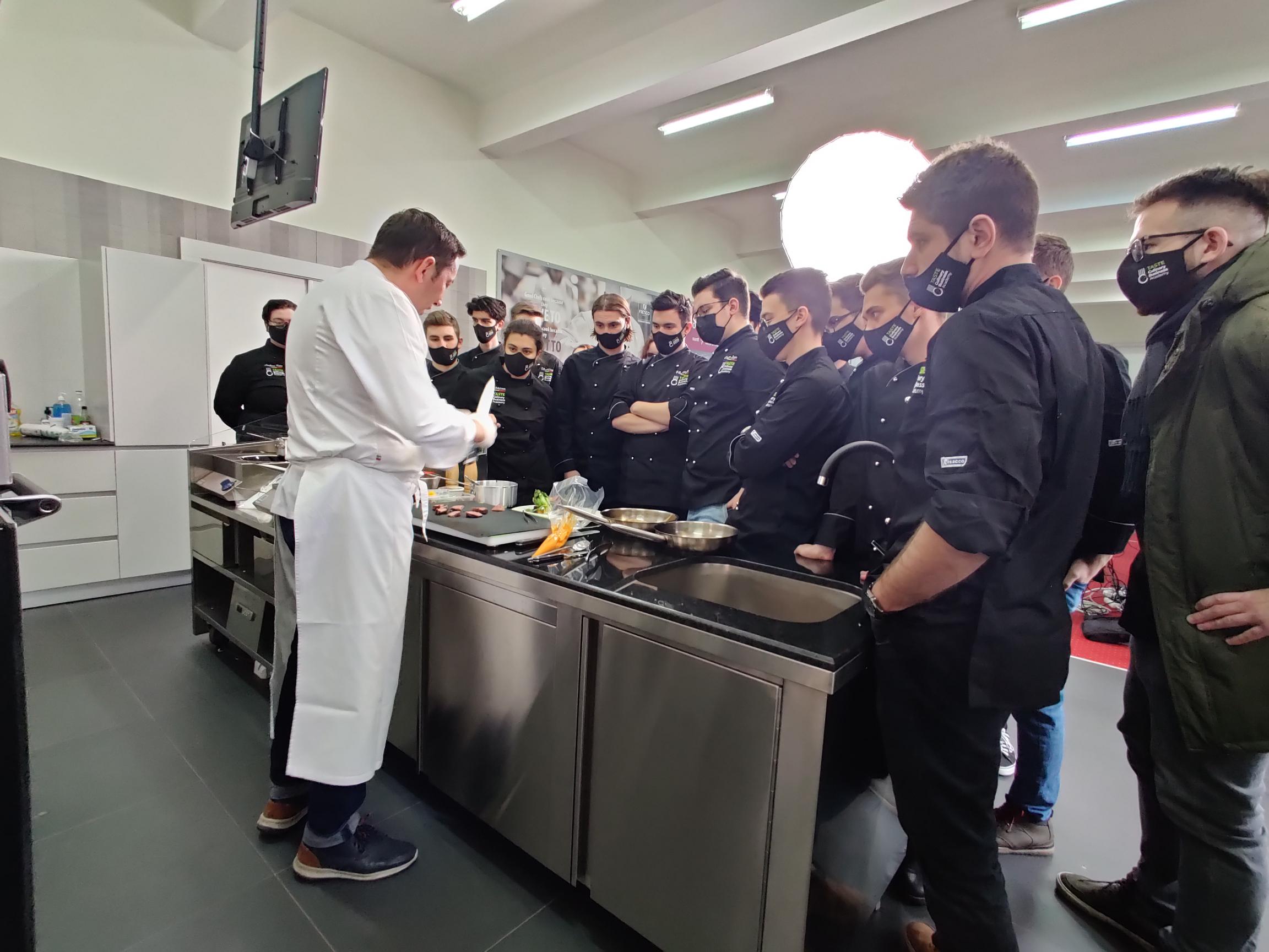 chef lecturer showing the class culinary techniques class gathered around a table in the show kitchen